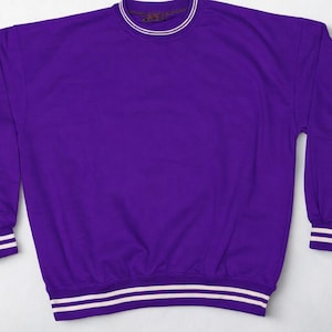 May include: A solid purple sweatshirt with white and purple striped cuffs and hem. The crew neck collar has a thin white stripe. The long-sleeved top is made of a soft material.