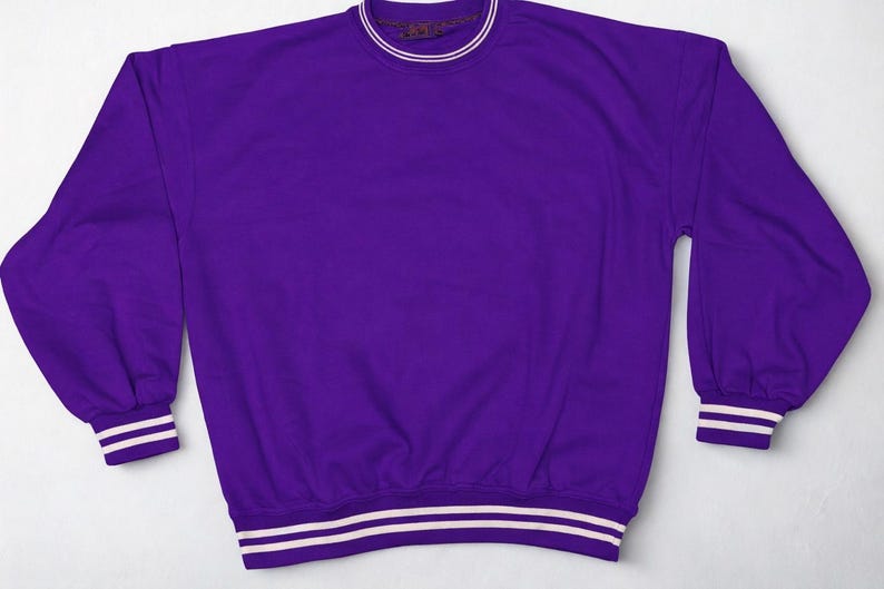 May include: A solid purple sweatshirt with white and purple striped cuffs and hem. The crew neck collar has a thin white stripe. The long-sleeved top is made of a soft material.