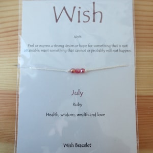 May include: White string bracelet with red and orange beads. The card says "Wish" and "July Ruby Health, wisdom, wealth and love". It also says "Wish Bracelet Close your eyes and make a wish. Tie the bracelet around your wrist or ankle. When your bracelet naturally breaks in two, your wish is ready to come true..."