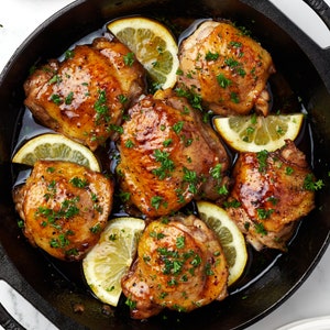 Honey butter chicken thighs with lemon slices in a skillet.