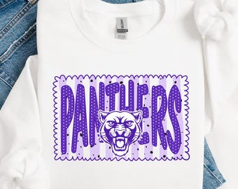 May include: A white long-sleeve sweatshirt featuring a rectangular graphic with a purple and white striped background. The graphic contains the word PANTHERS in large purple polka-dot letters with a snarling panther head replacing the letter H.