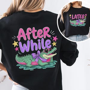 Könnte beinhalten: Schwarzes Sweatshirt mit einem Cartoon-Alligator, der eine herzförmige Sonnenbrille und eine Schleife trägt, mit dem Text "After While" und "Later". Der Alligator ist grün mit rosa Akzenten, vor einem Wasserhintergrund.