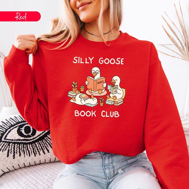 May include: A red sweatshirt featuring the words "SILLY GOOSE BOOK CLUB" and a graphic of three cartoon geese reading books. The geese are surrounded by small potted plants. The word "Red" is in a red rectangle in the upper left corner.