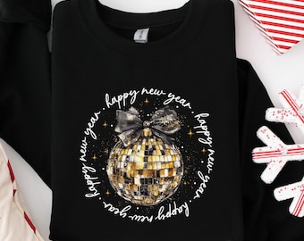 May include: Black sweatshirt featuring a gold and black disco ball design with a black bow. The words "happy new year" are written in a circular pattern around the disco ball. Festive holiday apparel.