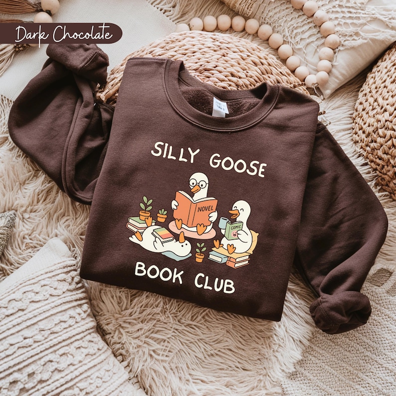 May include: Dark chocolate-colored sweatshirt with the text "SILLY GOOSE BOOK CLUB" and a graphic of cartoon geese reading books. The sweatshirt is made of a soft material and is perfect for book lovers.
