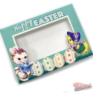 May include: A light blue card with the text "Happy Easter" in a white frame. The card has a cut-out window with a white bunny holding a blue and white egg and a yellow chick holding a basket of eggs. The background is a light blue with white polka dots.