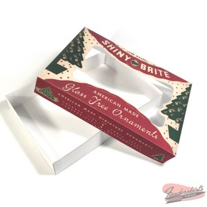May include: A red and green box with a clear plastic window. The box is labeled "Shiny Brite American Made Glass Tree Ornaments".