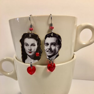 May include: A pair of earrings featuring images of Scarlett O'Hara and Rhett Butler from the movie Gone With The Wind. Each earring has a red heart-shaped crystal dangle.