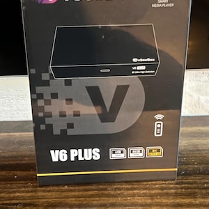 May include: Black box labeled "vSeeBox" with the text "V6 PLUS". The box features a graphic of a smart media player and includes icons for a remote, Wi-Fi, and 8K Ultra HD. It also lists 4GB RAM and 64GB ROM.