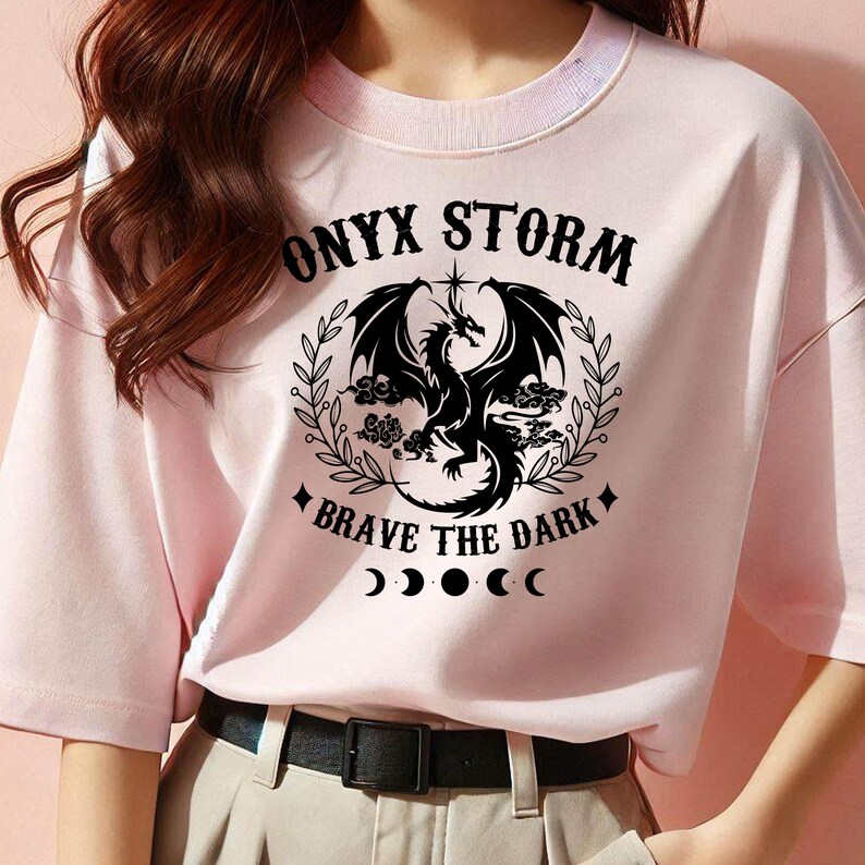 May include: Pink t-shirt with a black graphic of a dragon with the text "ONYX STORM" and "BRAVE THE DARK" with a crescent moon design.