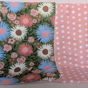 Pode incluir: Um cobertor revers&iacute;vel para beb&eacute;. Um lado tem um design floral com margaridas rosa, azuis e brancas sobre um fundo verde. O outro lado &eacute; rosa com bolinhas brancas. O cobertor &eacute; projetado para beb&eacute;s.
