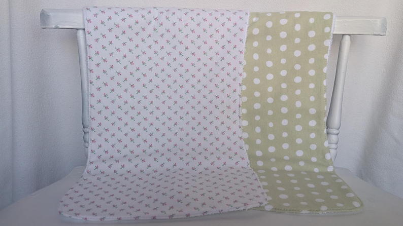 Pode incluir: Duas mantas de beb&eacute; drapeadas sobre uma cadeira branca. Uma &eacute; branca com um pequeno padr&atilde;o floral rosa. A outra &eacute; verde claro com grandes bolinhas brancas. As mantas s&atilde;o macias e provavelmente de algod&atilde;o.