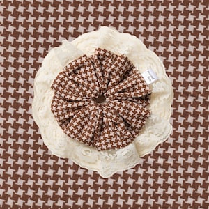 Peut inclure: Un chouchou marron et blanc à motif pied-de-poule avec une bordure en dentelle crème. Le chouchou est centré sur un fond à motif pied-de-poule marron et blanc. Le chouchou porte une étiquette "second lieu".