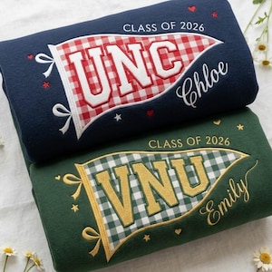 May include: Two folded sweatshirts, one navy blue and one green, with pennant designs. The navy sweatshirt has a red and white checkered pennant with "UNC" and "Chloe" embroidered. The green sweatshirt has a green and white checkered pennant with "VNU" and "Emily".