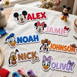 Op de afbeelding: Zes geborduurde stoffen patches met Disney-figuren en namen. De patches bevatten Mickey Mouse met de naam ALEX, Minnie Mouse met JAMIE, Donald Duck met NOAH, Goofy met JOHNSON, Pluto met NICK en Daisy Duck met de naam OLIVIA.