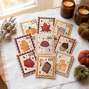Puede incluir: Una colección de nueve parches bordados cuadrados diseñados para parecer sellos postales. Cada parche presenta ilustraciones con temática otoñal que incluyen una calabaza, una hoja de arce, una taza de café, una hoja de roble, un hongo, una bellota, una boina, un libro y velas.