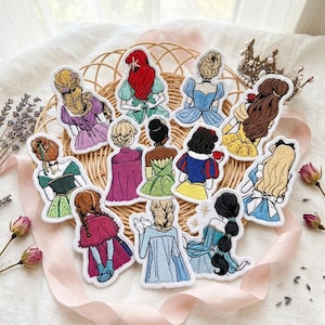 May include: A collection of twelve embroidered patches featuring the backs of various animated characters with distinct hairstyles and colorful outfits, arranged in a circular pattern on a woven wicker basket surface.