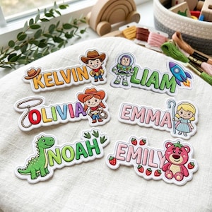 May include: Six embroidered name patches featuring cartoon characters and motifs. The patches display the names KELVIN, LIAM, OLIVIA, EMMA, NOAH, and EMILY, each accompanied by colorful stitched designs including a cowboy, space ranger, rocket, lasso, shepherdess, green dinosaur, and a pink bear with strawberries.