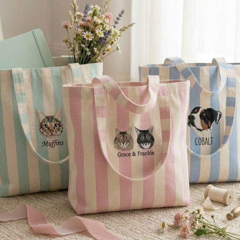 May include: Three striped tote bags with embroidered pet portraits. One bag is light blue and white with a cat and the name "Muffins". Another is pink and white with two cats and the names "Grace & Frankie". The third is blue and white with a dog and the name "Cobalt".