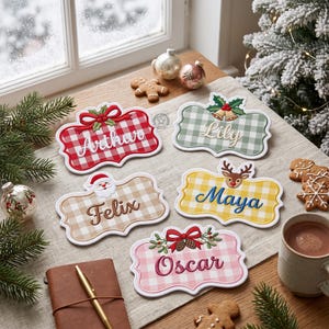 Op de afbeelding: Vijf decoratieve rechthoekige naamplaatjes met geschulpte randen en een gingham-patroon. De plaatjes zijn voorzien van de geborduurde namen Arthur, Lily, Felix, Maya en Oscar, versierd met feestelijke motieven zoals hulst, de Kerstman, een rendier en dennenappels.