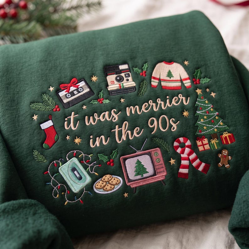 May include: A dark green sweatshirt featuring embroidered Christmas-themed 90s icons including a cassette tape, instant camera, television, and cookies. The text reads, "it was merrier in the 90s," surrounded by a Christmas tree, stocking, and scarf.