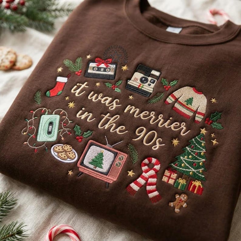 May include: A dark brown crewneck sweatshirt featuring embroidered Christmas-themed designs and the text "it was merrier in the 90s". The embroidery includes a cassette tape, a camera, a stocking, a sweater, a television, a scarf, and a tree.