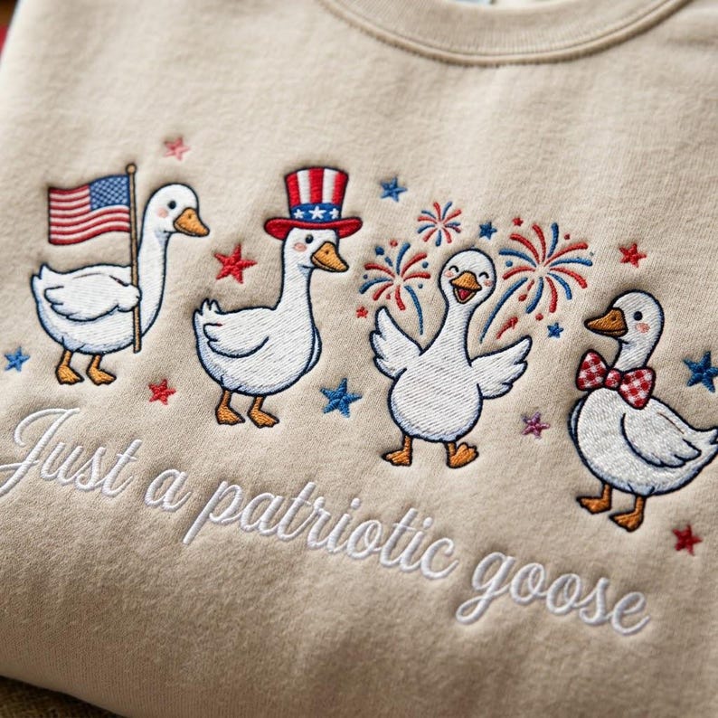 May include: Beige sweatshirt with embroidered patriotic geese. One goose holds an American flag, another wears a top hat, and a third has a bow tie. The text "Just a patriotic goose" is embroidered below.
