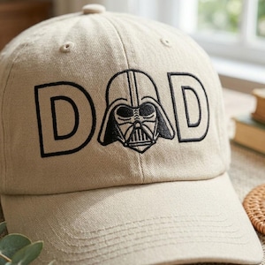 Può includere: Cappellino da baseball beige con la scritta "DAD" ricamata in nero, con una grafica di Darth Vader. Il cappellino ha una visiera curva e un bottone sulla parte superiore. Un accessorio alla moda per i fan dell'iconico film.