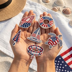 Op de afbeelding: Een verzameling van zes geborduurde patches met patriottische Amerikaanse vlagthema's, waaronder een zeeschelp, een reddingsboei, een zeilboot, een zeeschildpad, een kralenarmband met een sterbedel en een strandparasol in rood, wit en blauw.