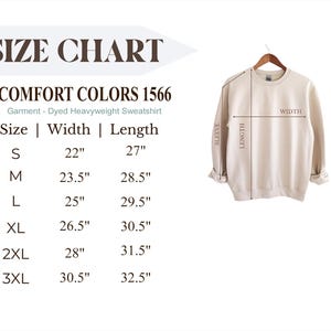 Puede incluir: Una sudadera crema Comfort Colors 1566 de peso pesado cuelga de una percha de madera. La imagen incluye una tabla de tallas con medidas en cm de ancho y largo, que van de la S a la 3XL. El texto dice "SIZE CHART".