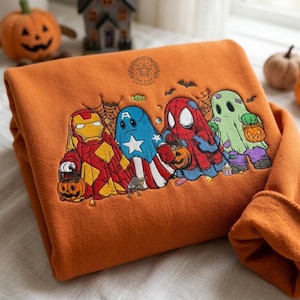 May include: An orange sweatshirt featuring an embroidered design of four characters dressed as ghosts for Halloween. The characters resemble Iron Man, Captain America, Spider-Man, and a classic ghost, each holding a pumpkin bucket. Text reads ONE STAR CROCHET.
