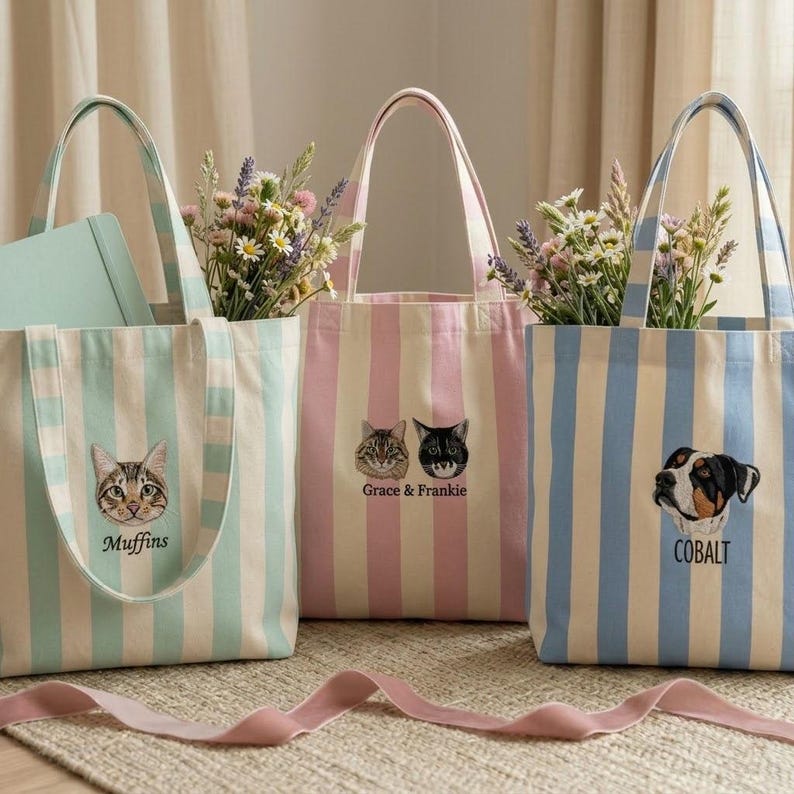 May include: Three striped tote bags with embroidered pet portraits and names. One bag is mint green and white with a cat and the name "Muffins". Another is pink and white with two cats and the text "Grace & Frankie". The third is blue and white with a dog and the name "Cobalt".