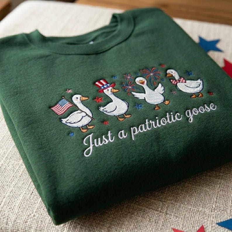 May include: A dark green sweatshirt with an embroidered design of four cartoon geese celebrating with fireworks, an American flag, and a patriotic hat. The text "Just a patriotic goose" is below the geese.