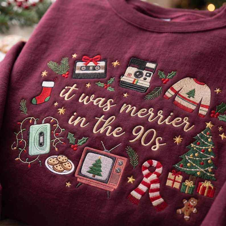 May include: A maroon sweatshirt featuring embroidered holiday-themed 90s icons including a cassette tape, instant camera, television with a tree, and cookies. The text "it was merrier in the 90s" is stitched in gold thread across the center.