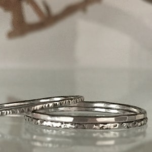 May include: Three silver stacking rings with a hammered texture. The rings are thin and delicate, and they are stacked on top of each other.