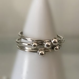 Puede incluir: Un anillo de plata con múltiples bandas y pequeñas cuentas redondas. El anillo está en un expositor blanco.