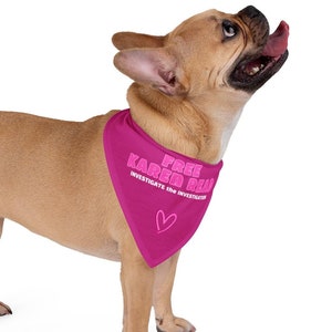 Könnte beinhalten: Ein hellbrauner Französischer Bulldogge trägt ein pinkfarbenes Halstuch mit dem Text "Free Karen Doll" und einem pinkfarbenen Herzen. Das Halstuch trägt auch den Text "Investigate and Invest".