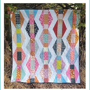 May include: A colourful quilt with a zigzag pattern, featuring diamond shapes in various colours and patterns. The quilt is hanging outdoors, with the word "Zigzag" at the top and "Kate Henderson Quilts" at the bottom.
