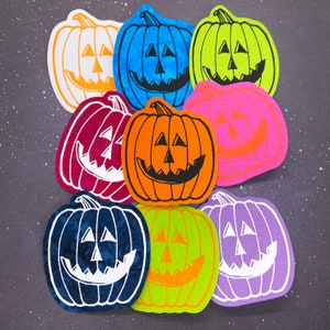 May include: Nine felt pumpkin patches in various colors, including orange, red, blue, green, and yellow. Each pumpkin has a different facial expression and is decorated with black paint.