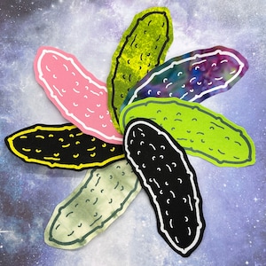 May include: A vibrant arrangement of pickle-shaped cutouts in a circular design. The pickles are in various colours, including pink, green, black, and tie-dye, each with a white outline. The background is a starry, galaxy-themed design.