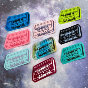 May include: Ten colorful cassette tape stickers with a retro design. Each sticker features a different color and design, including blue, pink, green, purple, and black.