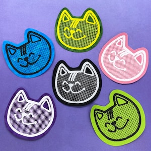 May include: Six iron-on patches featuring smiling cats in various colors, including blue, green, black, pink, purple, and lime green. The cats have a pixelated design and are all smiling.