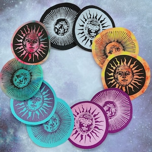 May include: A collection of circular patches featuring a sun design with a face. The patches are in various colors, including black, orange, purple, and teal, with a tie-dye effect on some. The sun's rays and face are in a contrasting color.