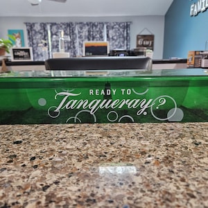 May include: A rectangular, translucent green plastic storage container featuring the white text "READY TO Tanqueray?" printed on the front side, accompanied by a graphic design of several white circles of varying sizes.