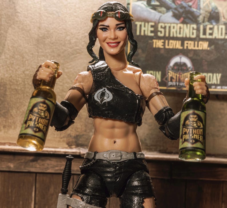 May include: A woman action figure holding two bottles of Python Pilsner beer. The figure is wearing a black leather vest with a Cobra logo, black pants, and goggles. The background is a brick wall with a sign that reads "The Strong Lead. The Loyal Follow."