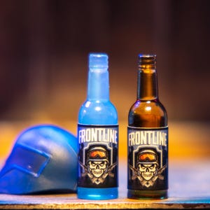 May include: Two small glass bottles with blue and brown liquid. Both bottles have a black and white label with a skull and crossbones graphic and the word "FRONTLINE" printed on them.