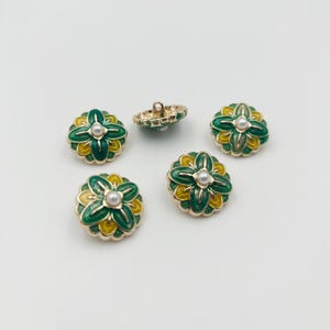 May include: A collection of decorative buttons with a floral design. The buttons feature a gold-colored metal rim, with green and yellow enamel petals. Each button has a faux pearl center. One button is turned over, showing the shank.