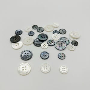 May include: Assortment of white, black, and iridescent buttons with four holes each. The buttons are made of mother of pearl and are various sizes.