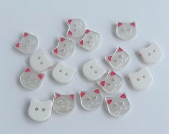 May include: A collection of cat-shaped buttons. The buttons are white with a translucent appearance, featuring pink accents on the ears and whiskers. Each button has two small holes for sewing.
