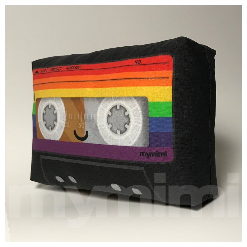 May include: A black cassette tape pillow with a rainbow design and the text "mymimi" on the bottom. The cassette tape has a smiling face.